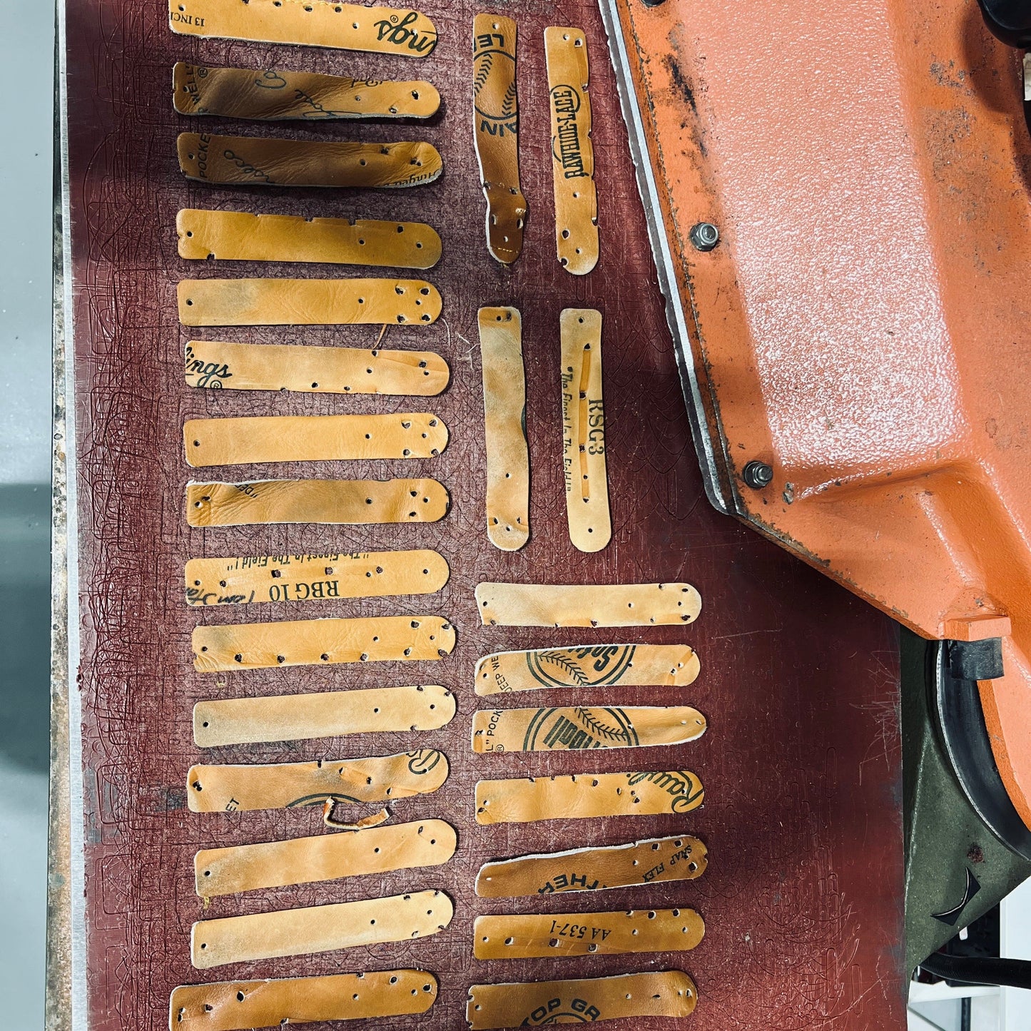 Several worn leather patches and strips labeled "Wanderchain" and "Baseball Glove" laid out on a red work surface.