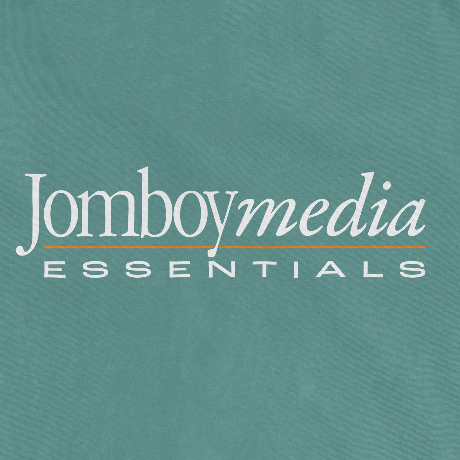 Close-up of a teal T-shirt with "Jomboy media ESSENTIALS" printed in white and orange text, representing a retro-inspired design.