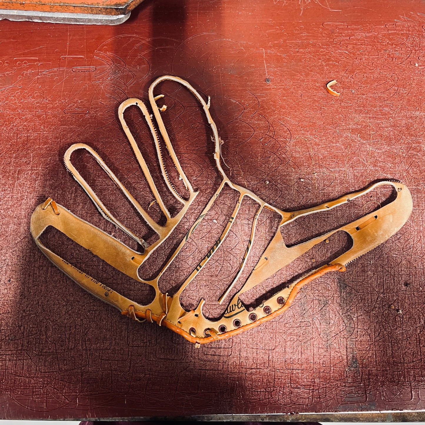 A disassembled baseball glove with a Wanderchain logo, showing its leather frame and internal structure on a red work surface.