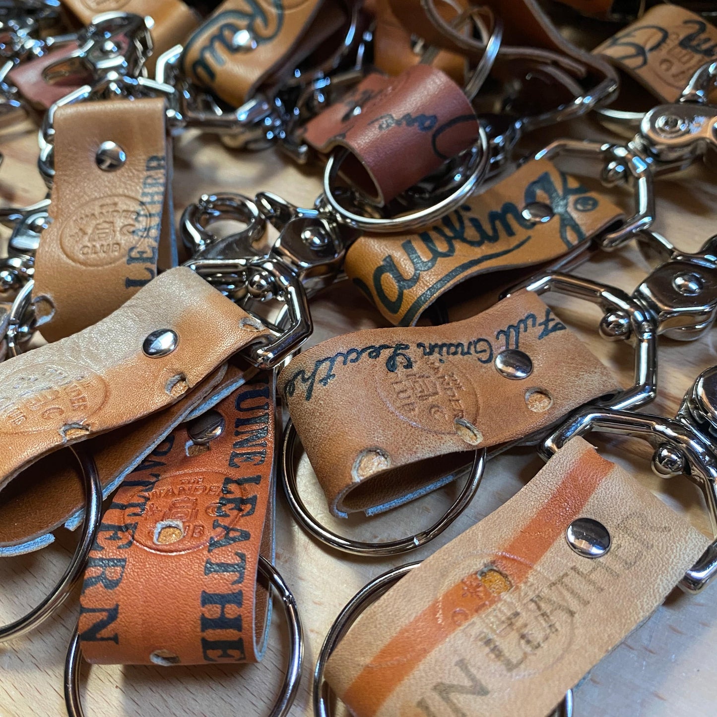 Close-up of vintage leather and metal Wanderchain baseball glove keychains with engraved branding, scattered on a wooden surface.