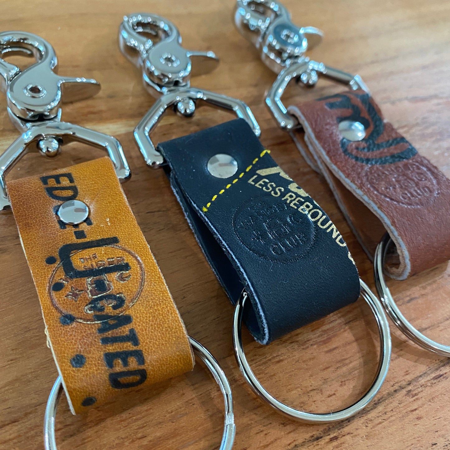 Three leather and metal keychains with baseball glove and Wanderchain branding, featuring colorful straps and metal rings.