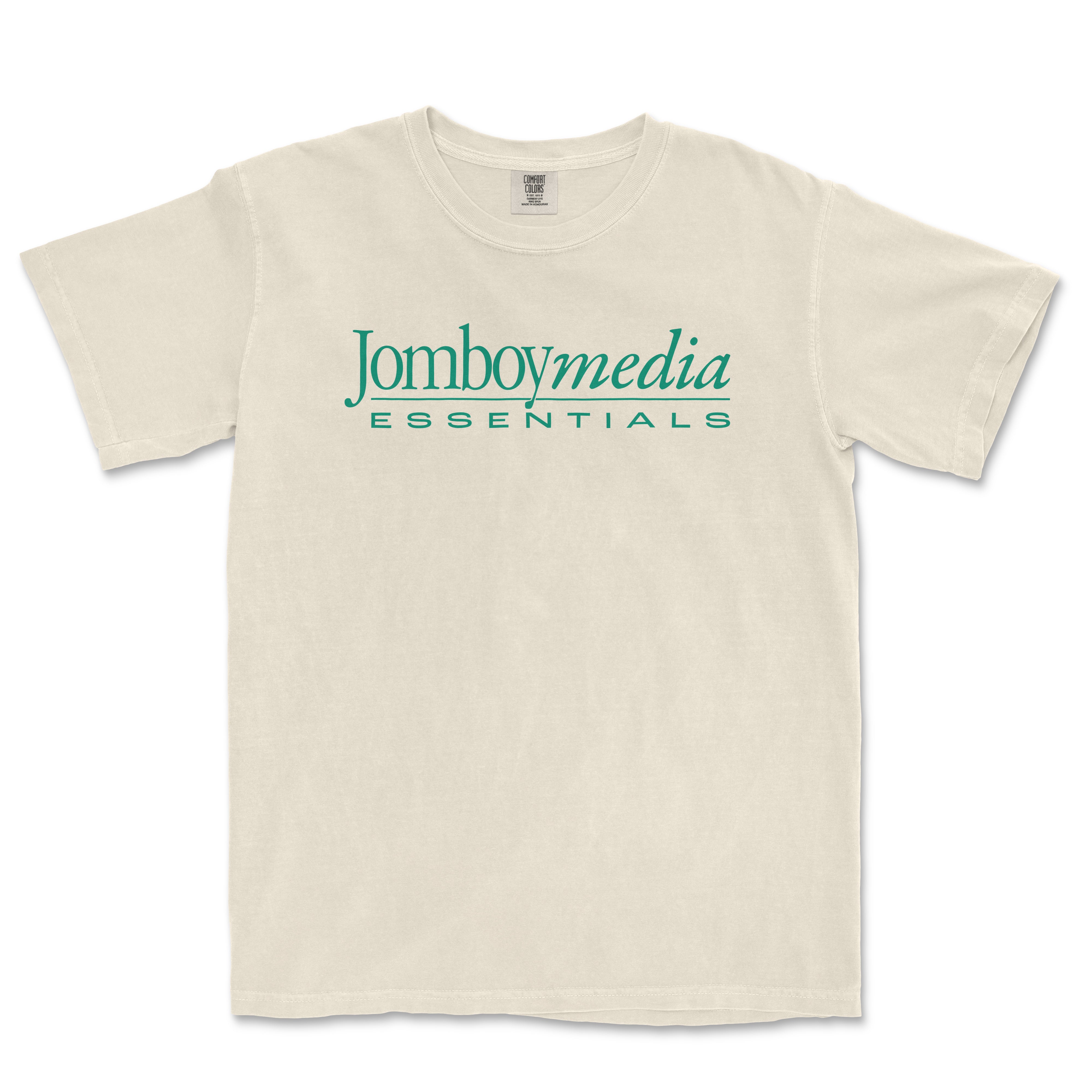 Beige T-shirt with "Jomboymedia Essentials" logo in teal text across the front, vintage-inspired design, casual style.
