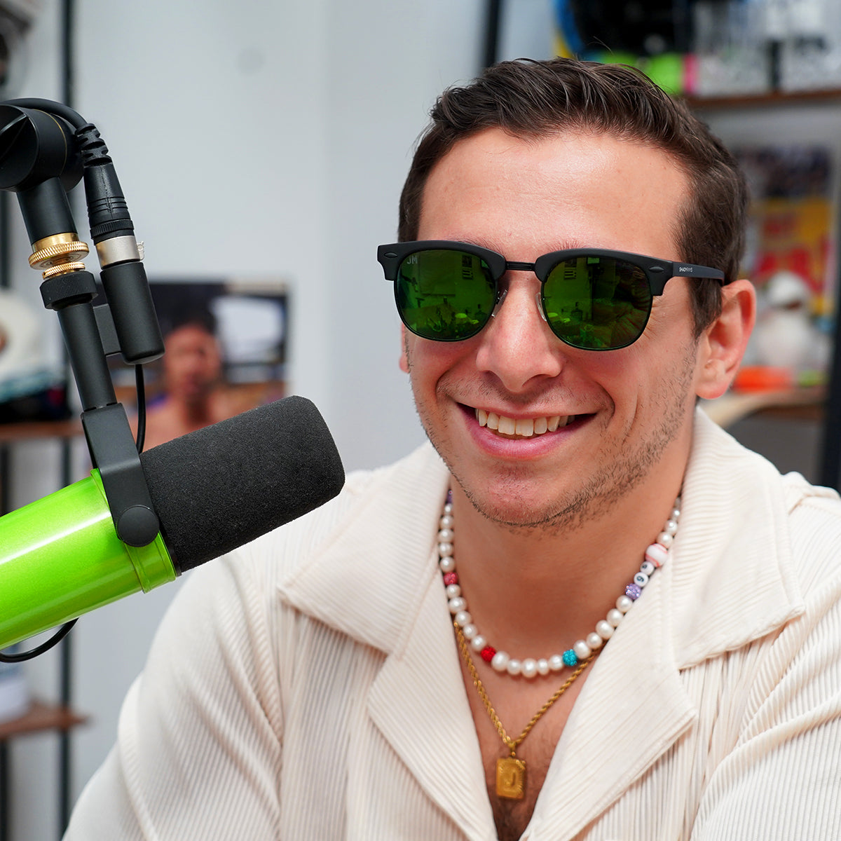 Man wearing Shady Rays The Jake sunglasses with green lenses, smiling in front of a microphone during a recording session.