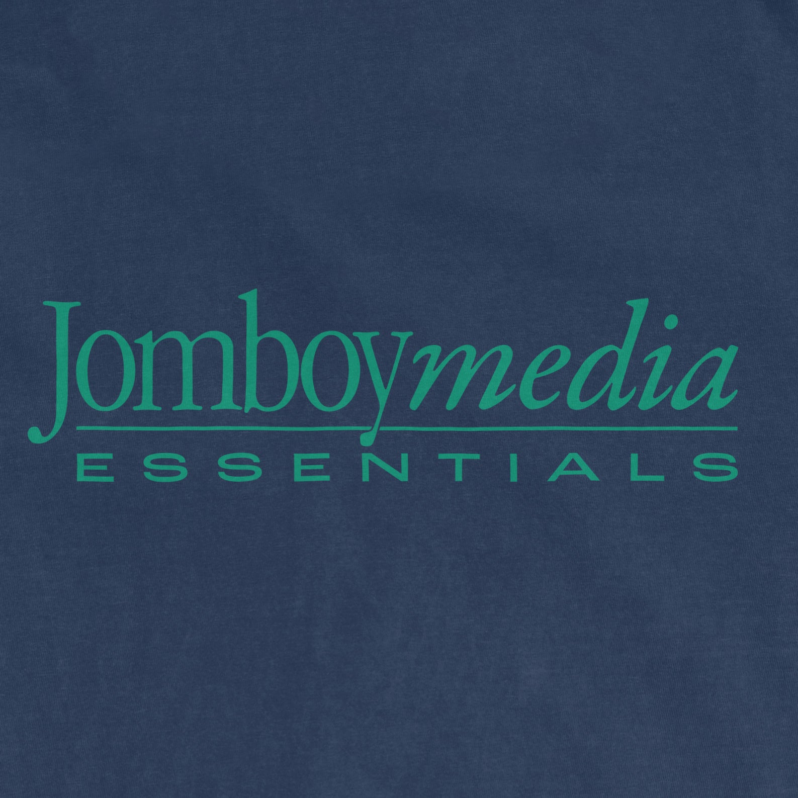 Close-up of a navy blue fabric with green text reading "Jomboymedia Essentials" in a stylish font.
