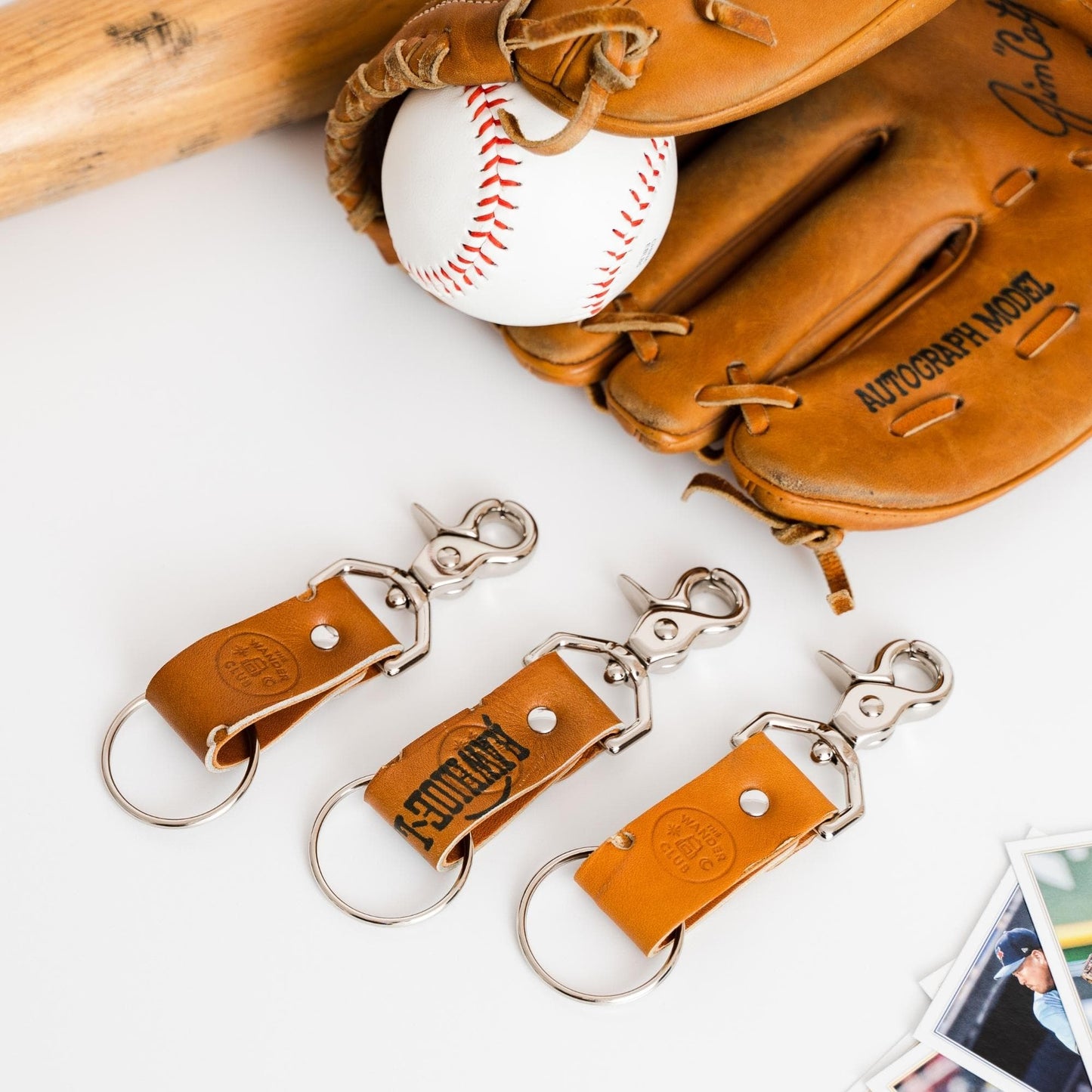 Leather baseball glove with a white baseball and three Wanderchain keychains featuring metal clips and leather straps.