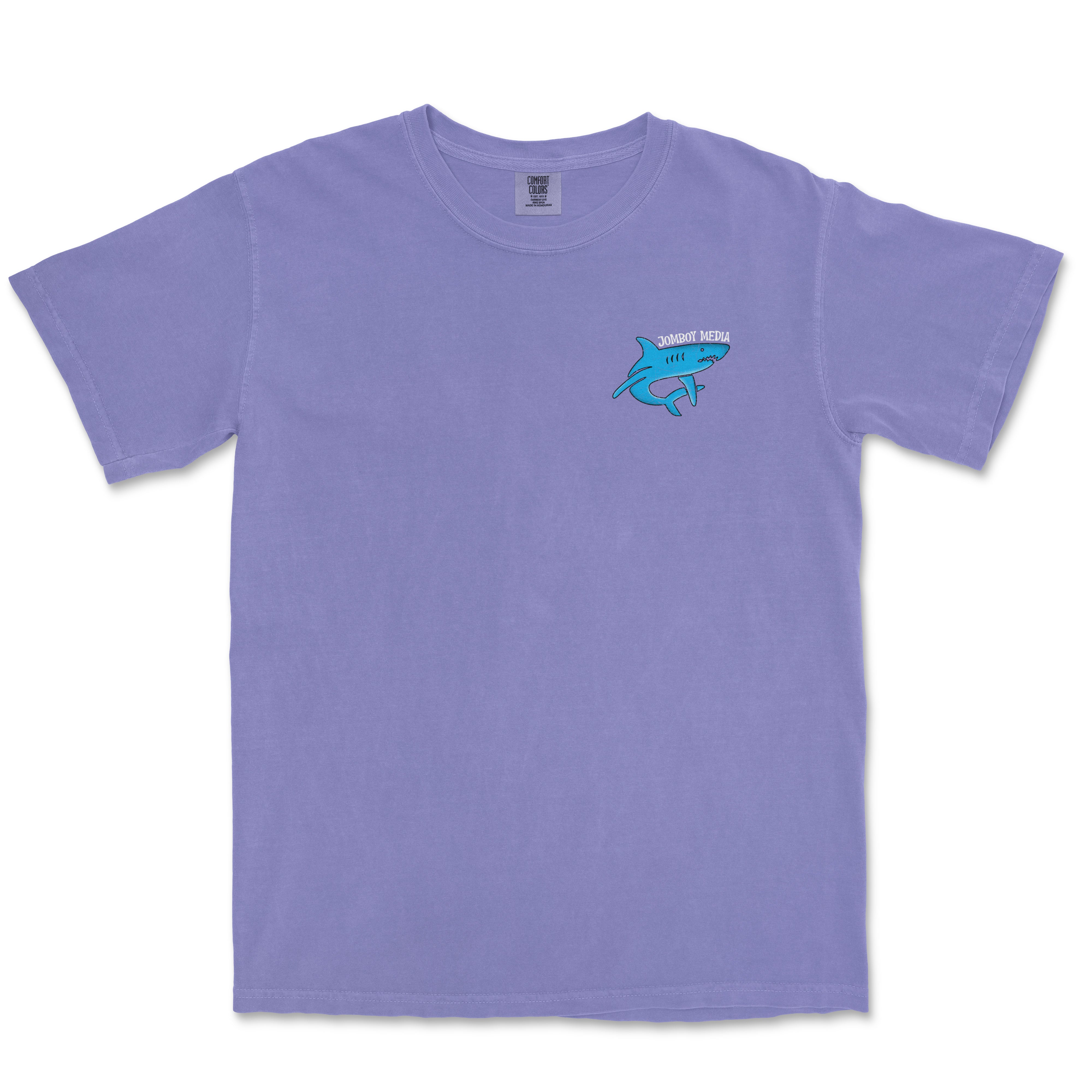 Lavender Comfort Colors tee featuring a small embroidered blue shark and "Jomboy Media" text on the upper left chest.