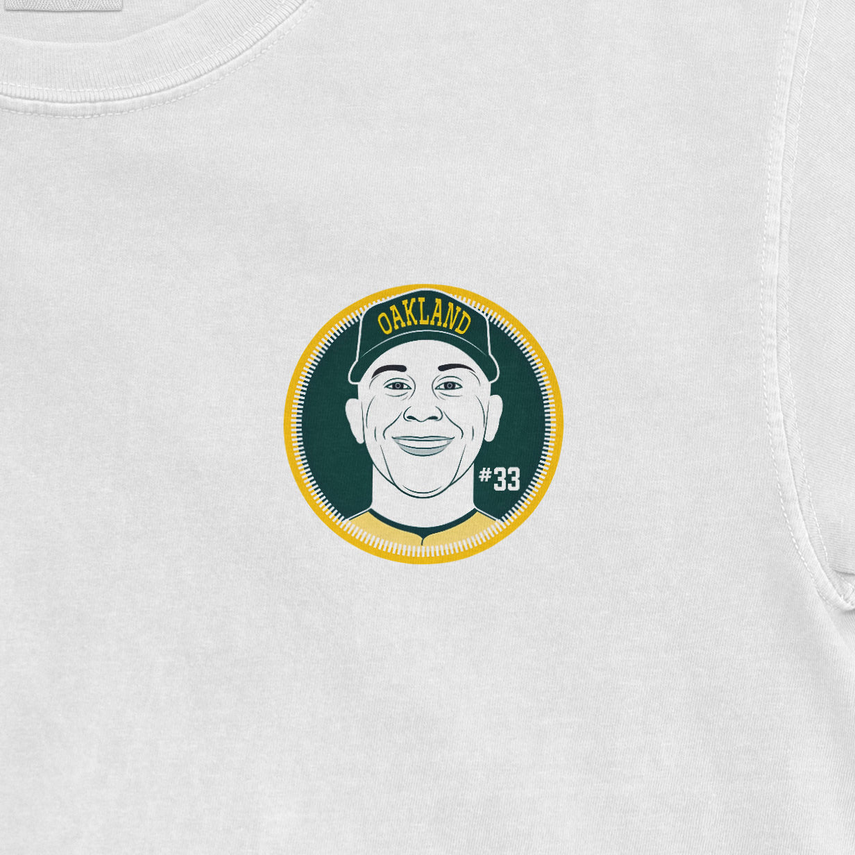 White Comfort Colors tee featuring a circular graphic of a smiling person wearing a cap with "OAKLAND" and "#33" text.