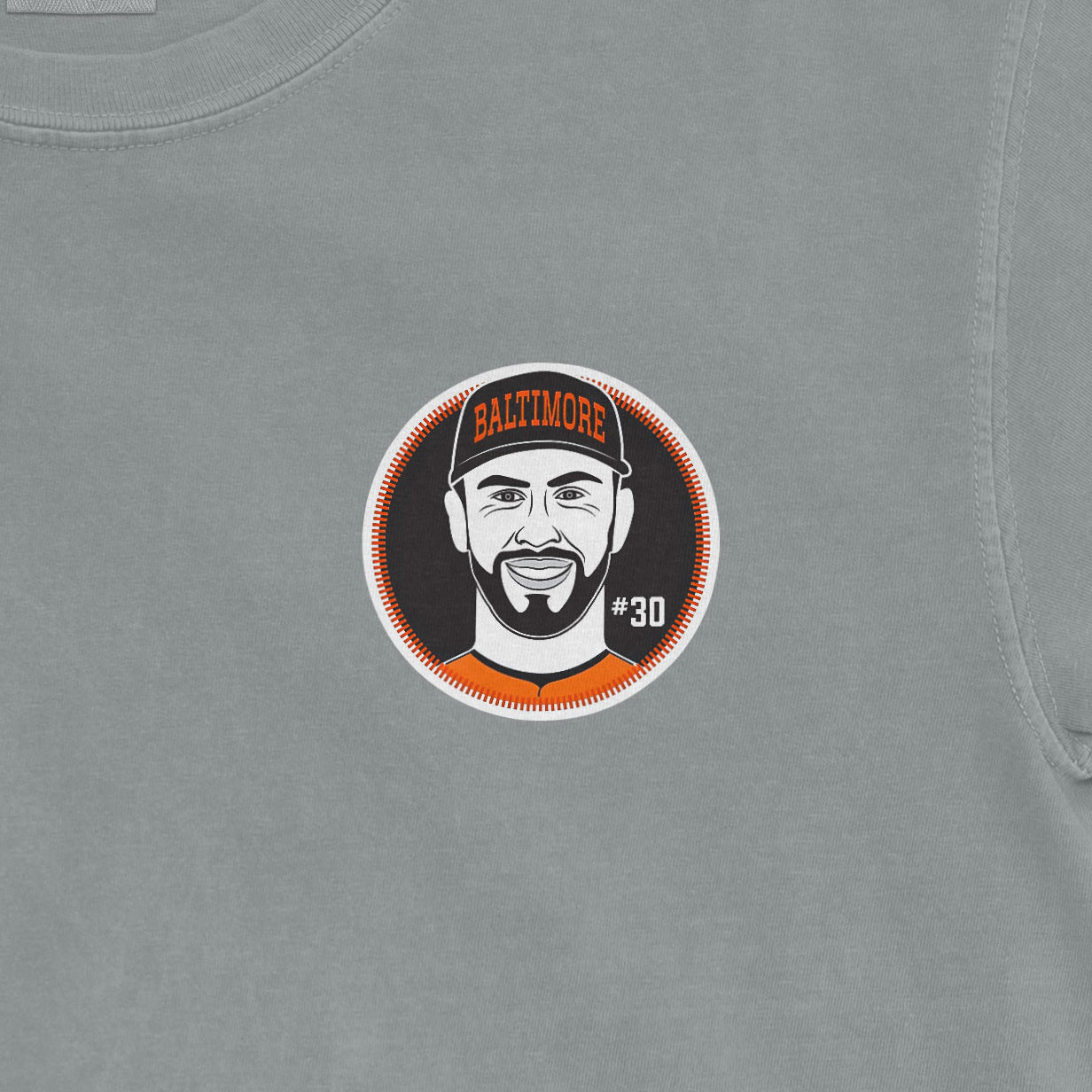 Close-up of a Comfort Colors tee featuring a graphic of a smiling man wearing a Baltimore cap, with "#30" on a gray fabric background.