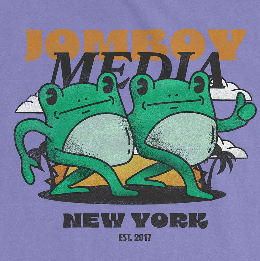 Comfort Colors tee featuring a playful graphic of two frogs with "Jomby Media" text, "New York" and "Est. 2017" on a purple background.
