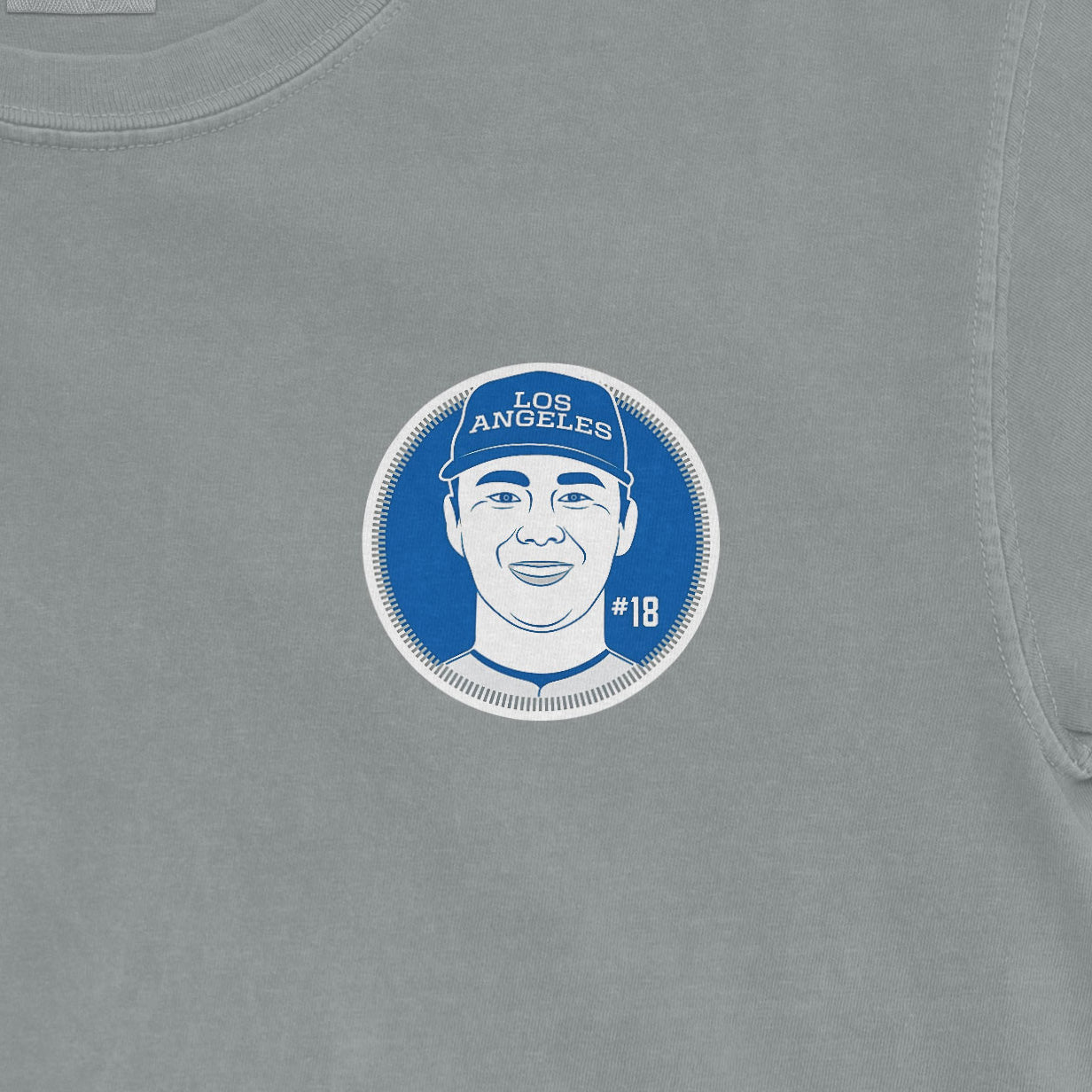 Close-up of a gray shirt featuring a circular graphic of Yoshinobu Yamamoto with "LOS ANGELES" cap, #18, smiling face illustration.