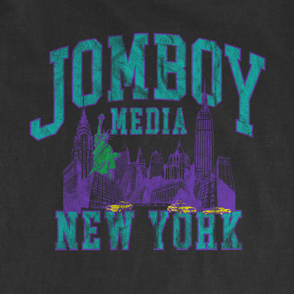 Vintage-style black Comfort Colors T-shirt featuring a neon purple and green graphic of New York City landmarks, with "JOMBOY MEDIA 90'S EDITION" text.