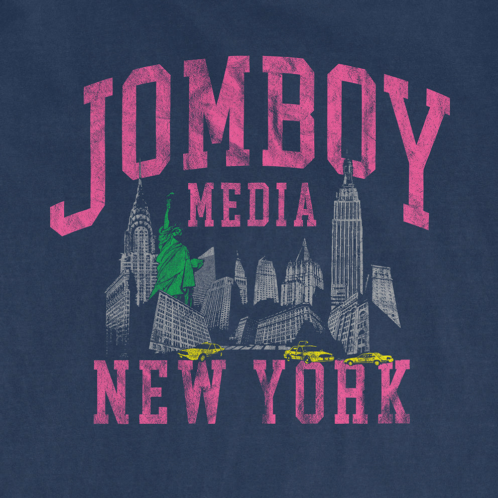 Comfort Colors tee featuring a vintage-style graphic of New York City skyline, Statue of Liberty, and yellow taxis with "JOMBOY MEDIA 90'S EDITION" in bold pink text.