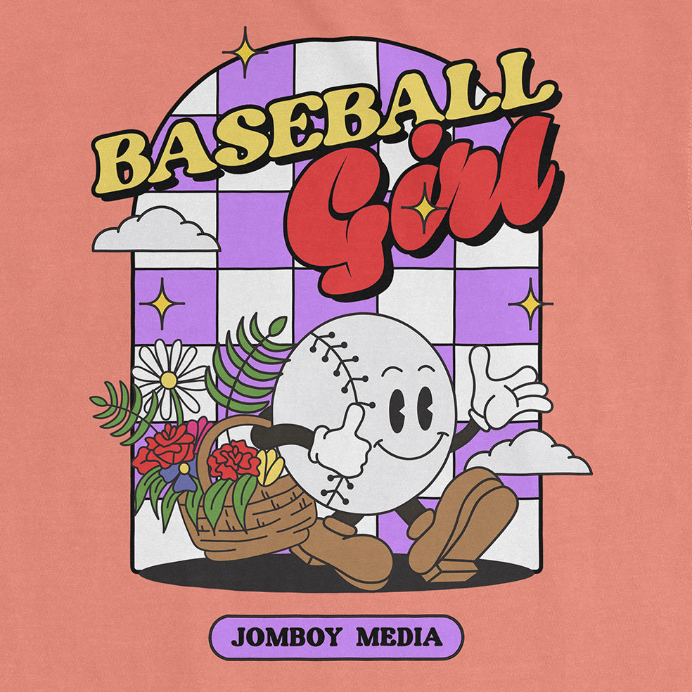 A Comfort Colors tee featuring a cartoon baseball character with a smiling face, holding a basket of flowers, and playful text "Baseball Girl" above.