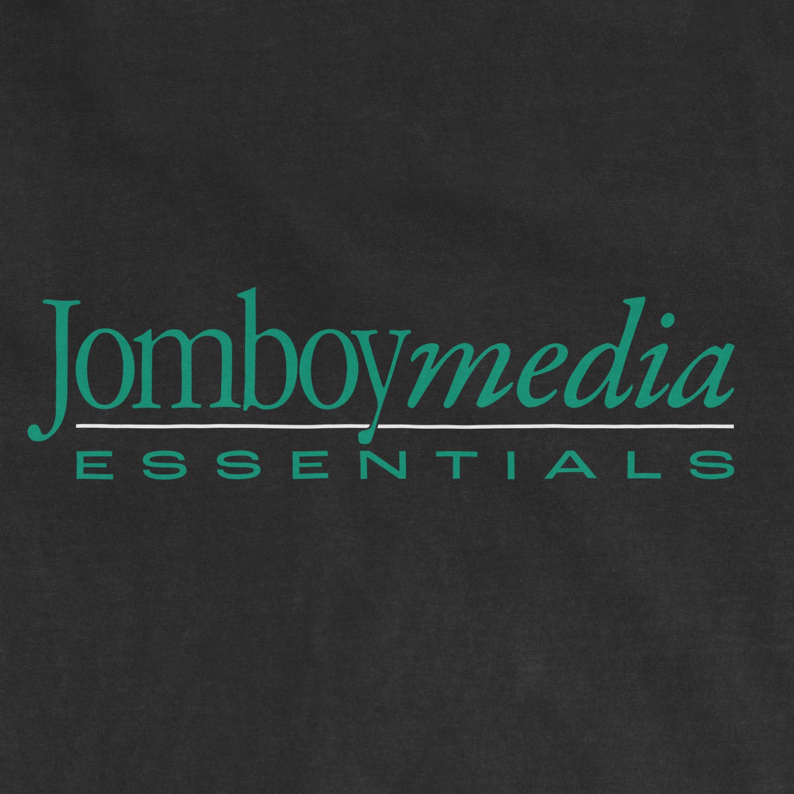 Close-up of a black fabric with teal and gray text reading "Jomboy Media Essentials," highlighting a modern, stylish logo design.