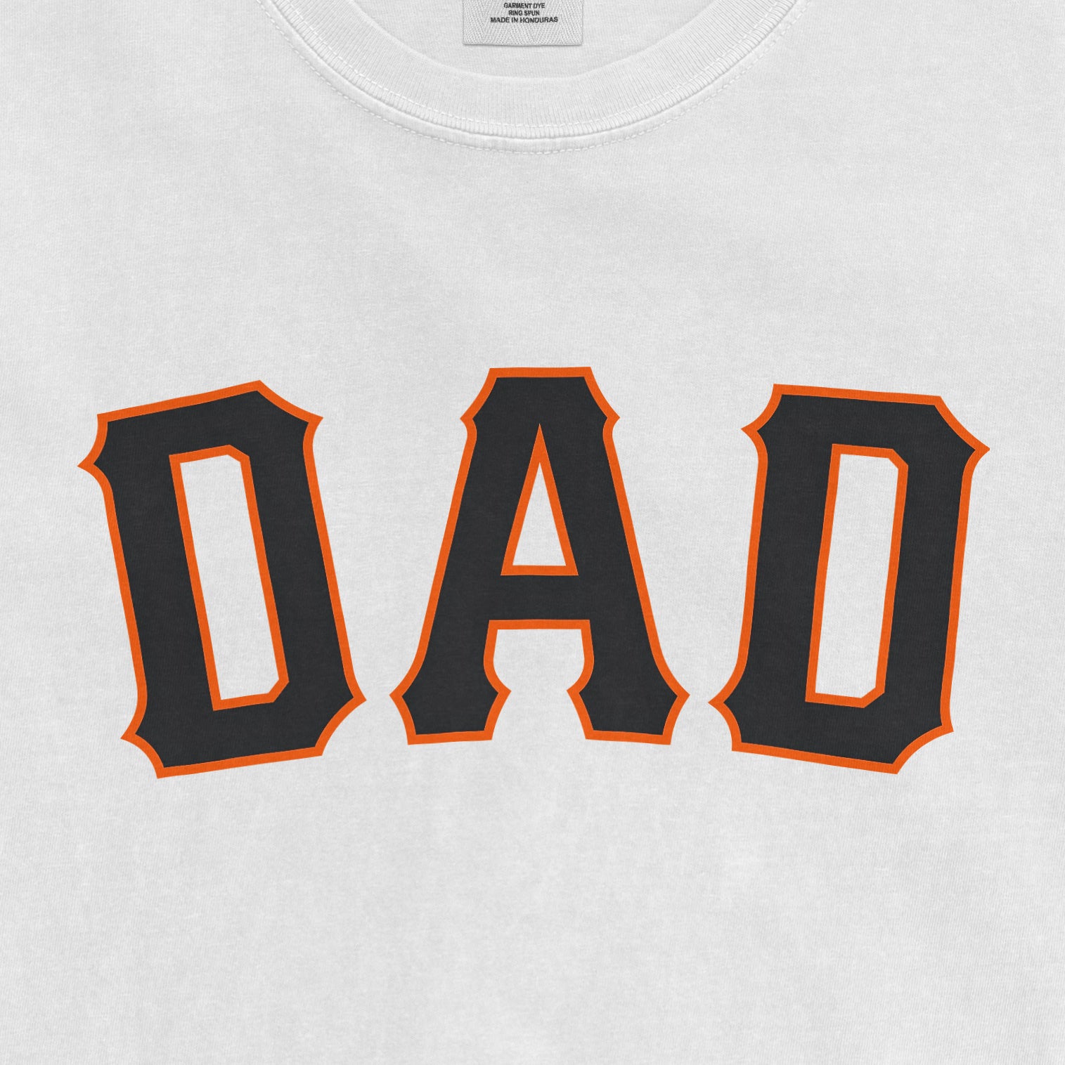 Close-up of a white T-shirt with "DAD" printed in bold black letters outlined in orange, celebrating San Francisco baseball dads.