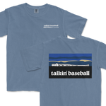 Light blue T-shirt featuring a small "talkin' baseball" logo with a baseball bat and ball on the front, and a larger graphic of a baseball bat and ball against a stylized landscape on the back.