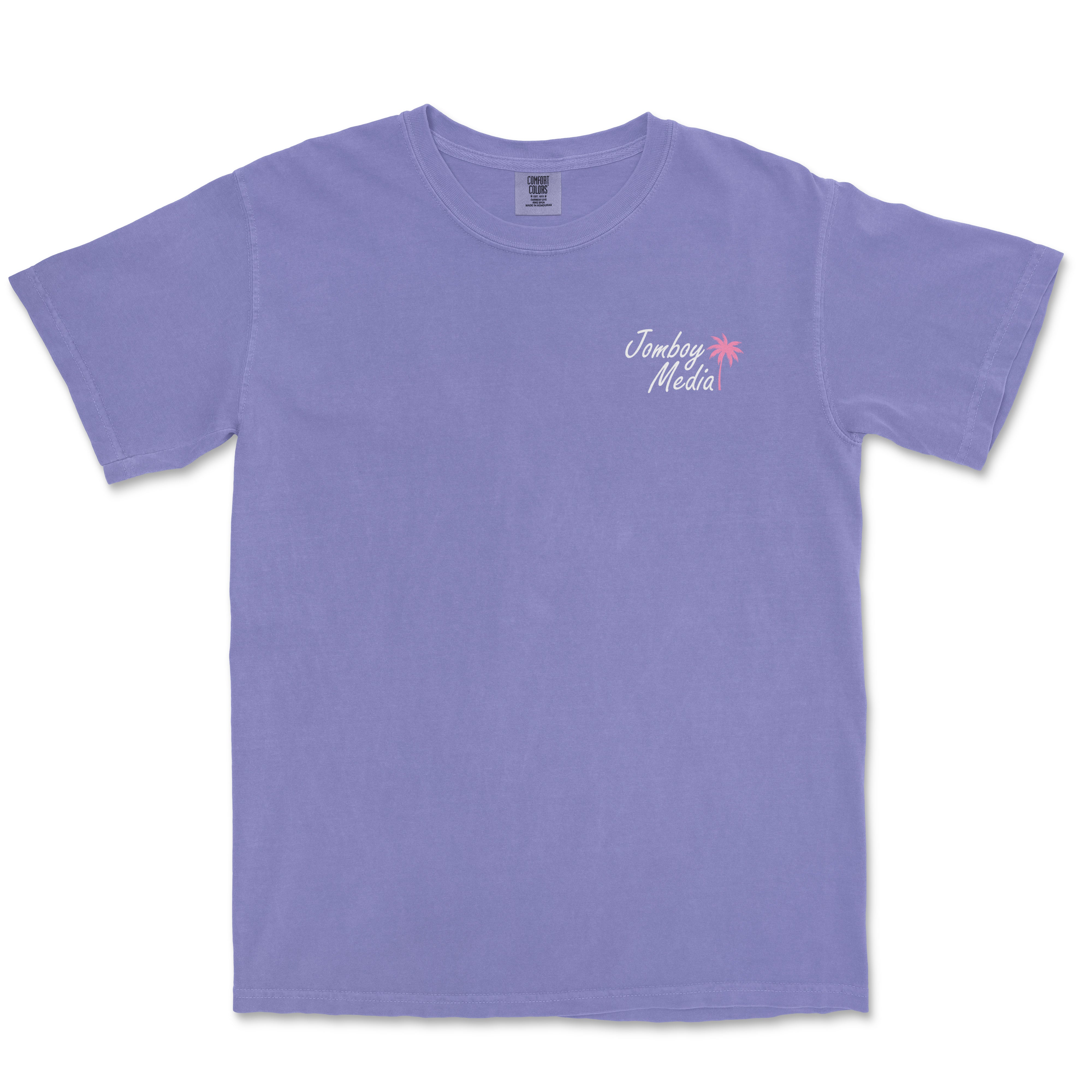 Lavender Comfort Colors T-shirt featuring "Greetings from Jomboy Media" text with a pink palm tree graphic on the front.