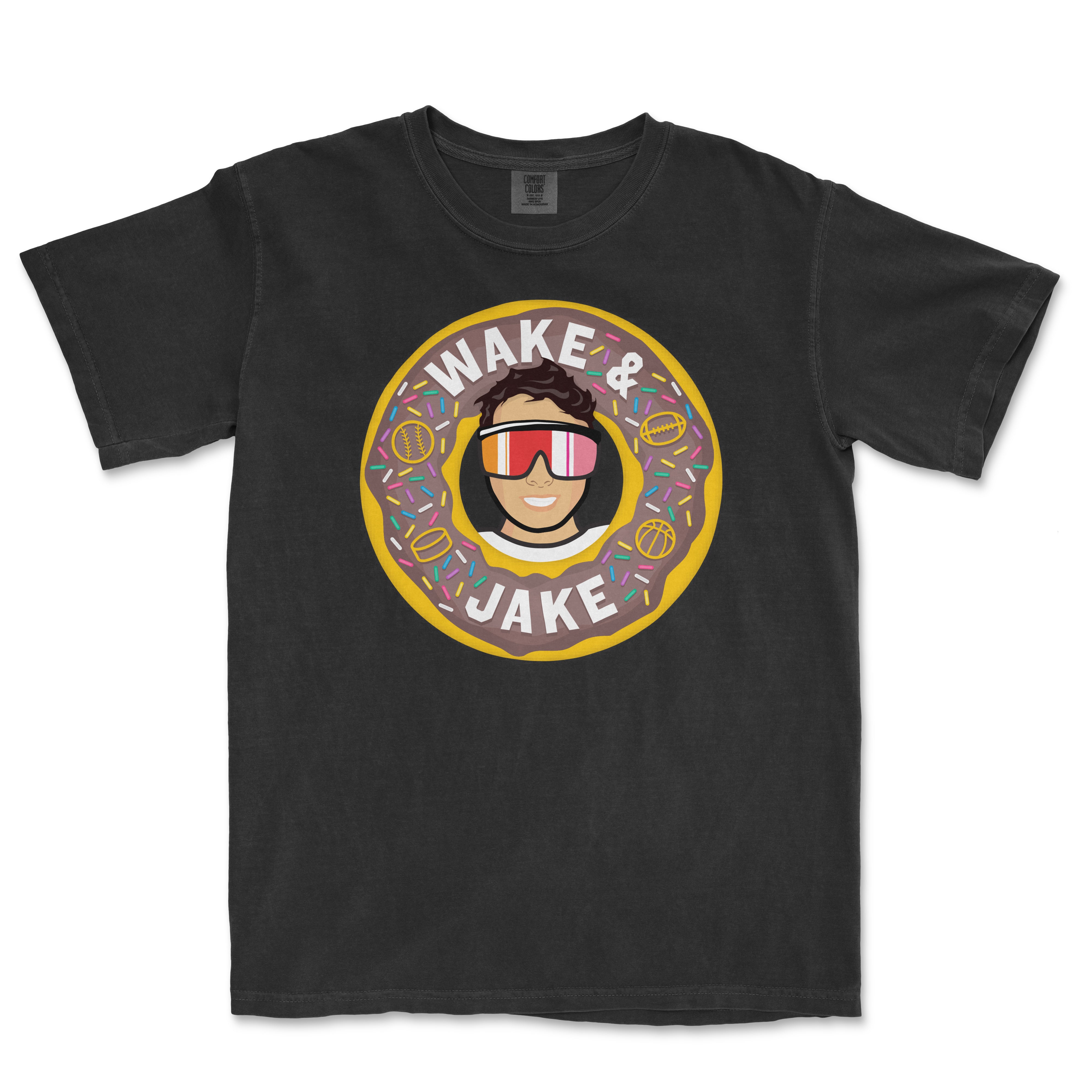 Black T-shirt featuring a cartoon illustration of a person wearing sunglasses inside a donut with colorful sprinkles, and the text "Wake & Jake".