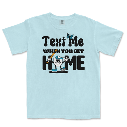 Light blue T-shirt with a cartoon character holding a bat, and text that reads "Text Me When You Get Home" in playful black font.