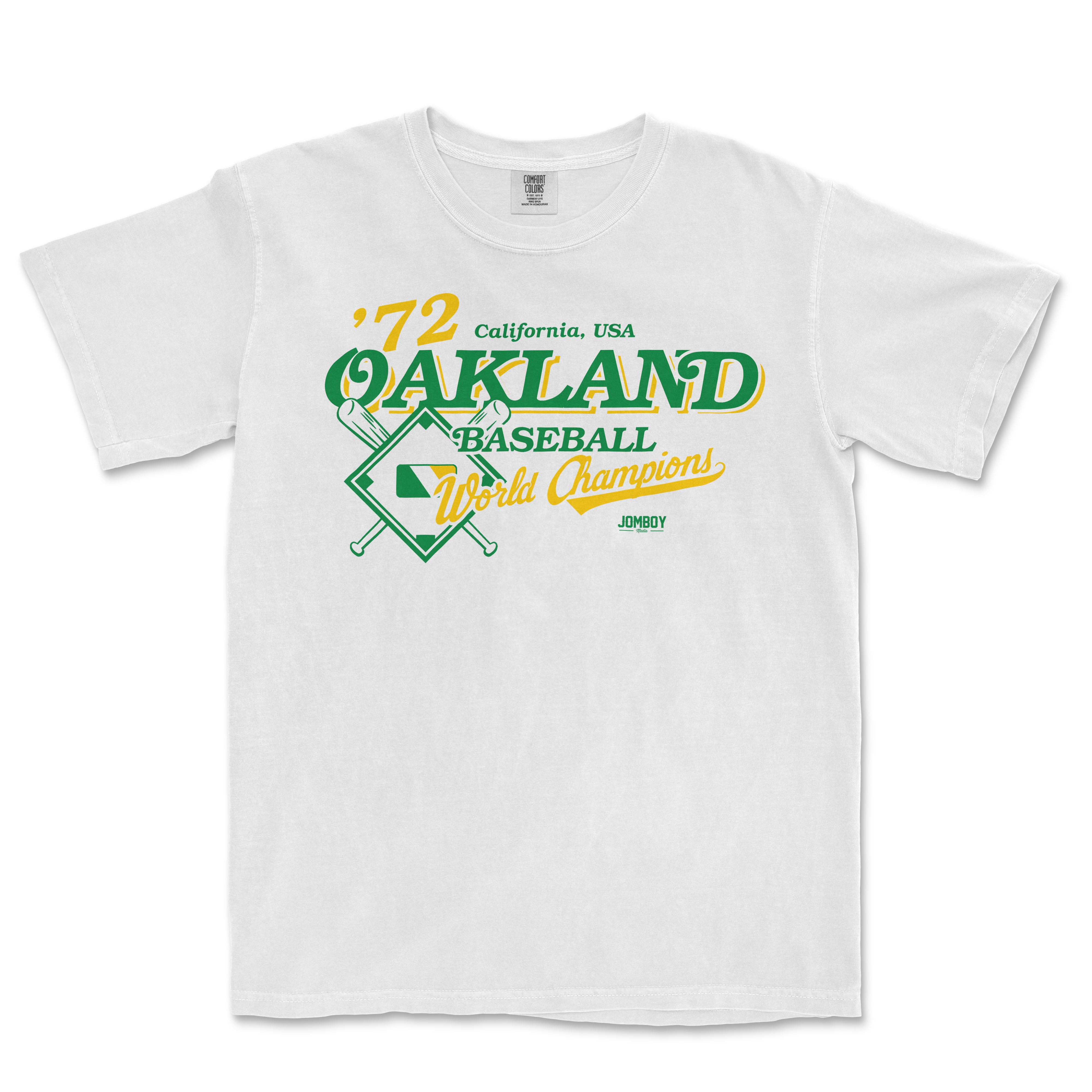 White Comfort Colors tee featuring vintage Oakland baseball team design with green and yellow text, crossed bats, and "World Champions" slogan.