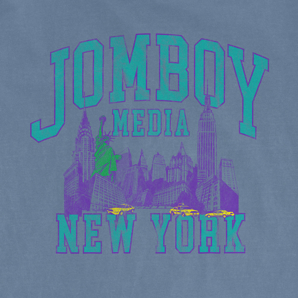 Comfort Colors tee featuring a vintage-inspired graphic of New York City with the text "JOMBOY MEDIA 90's Edition" in bold, colorful letters.